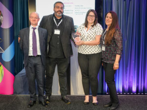 A photo of 4 people on stage collecting an award. They are facing the camera and smiling.