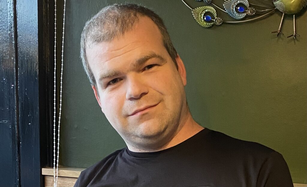 Head and shoulders image of a man wearing a black t-shirt.